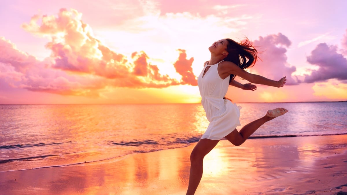 Happy well being free woman jumping of happiness at beach sunset enjoying life in serene picturesque sunset at the ocean . Aspirational happy lifestyle with pretty young Asian lady enjoying freedom.