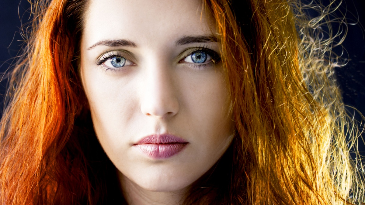 Portrait of a calm pensive young beautiful girl woman with long hair and blue eyes. Model posing in studio on dark background.