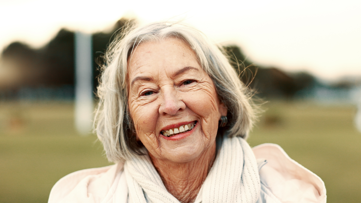 Face, elderly woman and happy in nature on vacation, holiday or travel in winter. Portrait, smile and person in the countryside, park or garden for wellness, freedom and wind in hair in retirement.