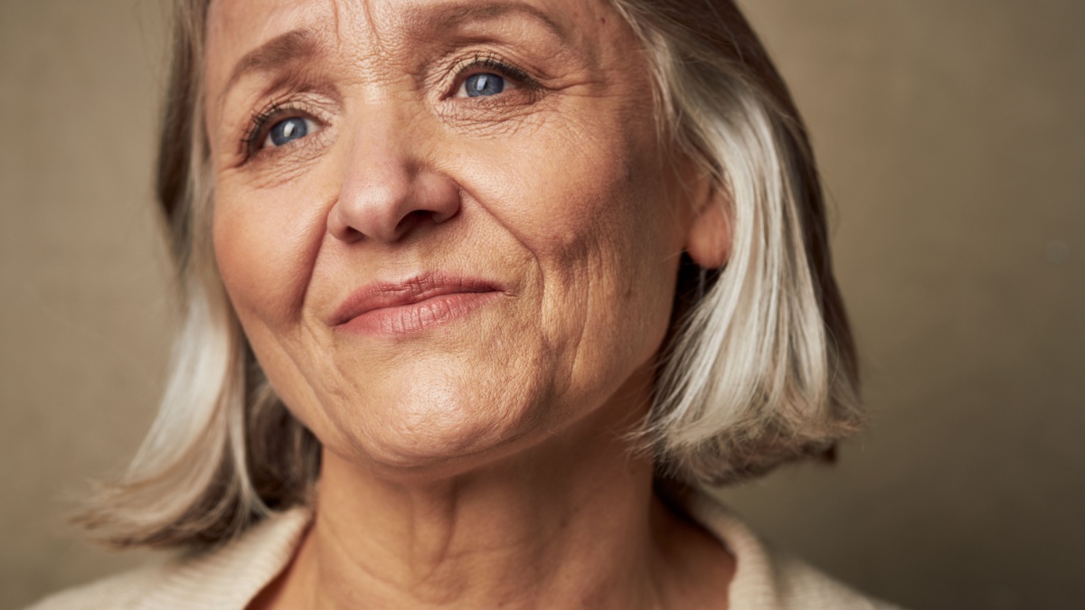 Elderly woman face closeup makeup gray background.