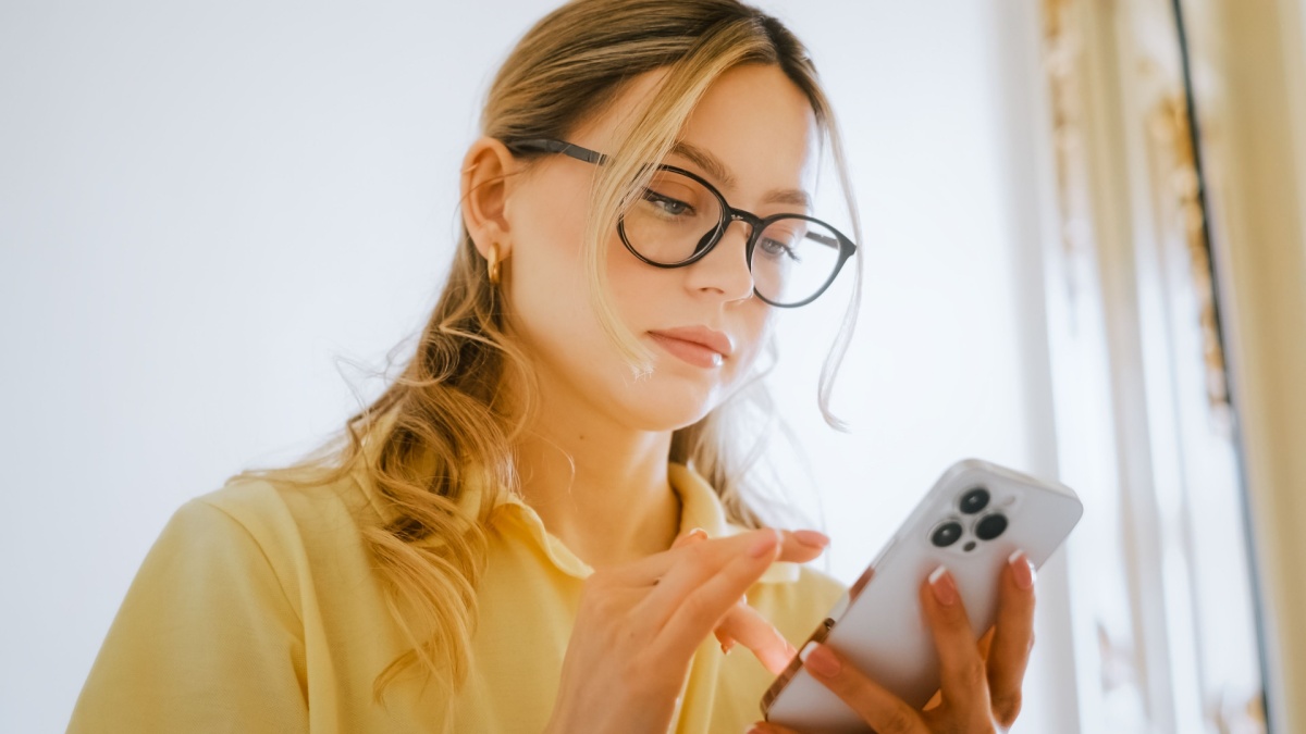 Happy smiling young attractive caucasian woman in eyeglasses using mobile phone at home.