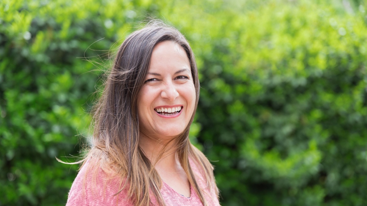 Outdoor portrait of a laughing 45 year old woman with windblown brown hair looking at the camera in the park on a sunny day. Confidence and tranquility of a mature woman. Happiness, lifestyle.