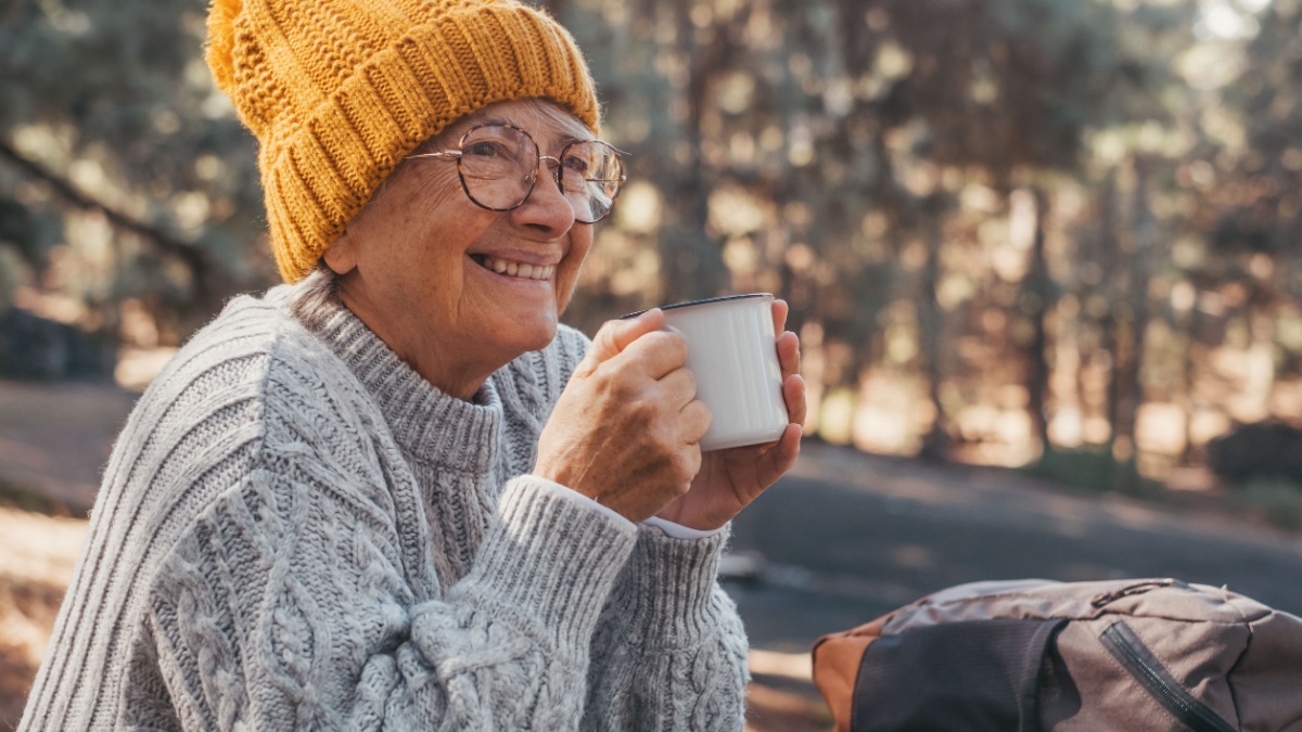 Head shot portrait close up of middle age woman relaxing drinking coffee or tea sitting at table in the forest of mountain in the middle of nature. Autumn season enjoying concept lifestyle..