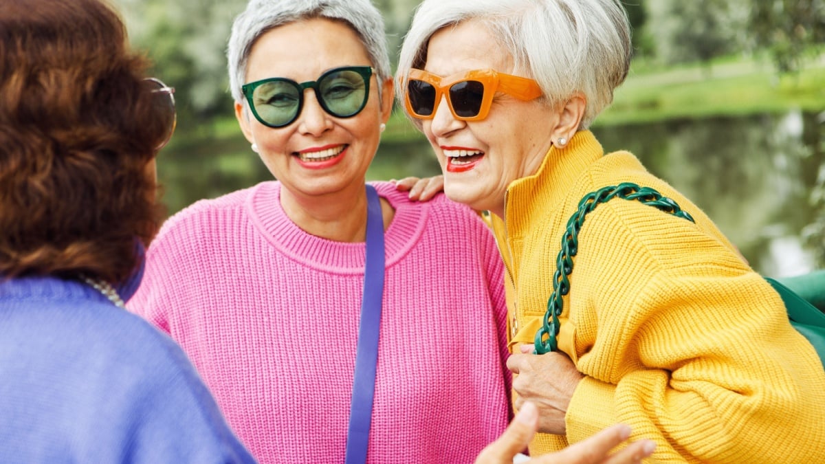 Pensioner female friends meet in the park, chatting and laughing merrily. Friendship, people and golden age concept.