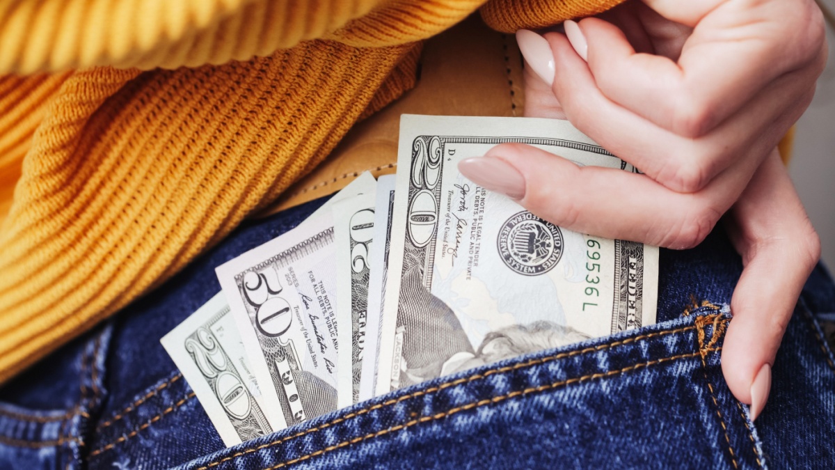 Pocket money background. Dollar bills in rear pocket. Woman in blue jeans. Sexy girl in trousers. Female butt. Female butt in jeans. American style fashion. Hand reaching for money.
