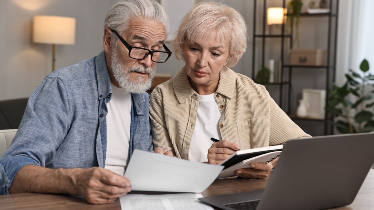 Pension savings. Senior couple planning budget at wooden table indoors.