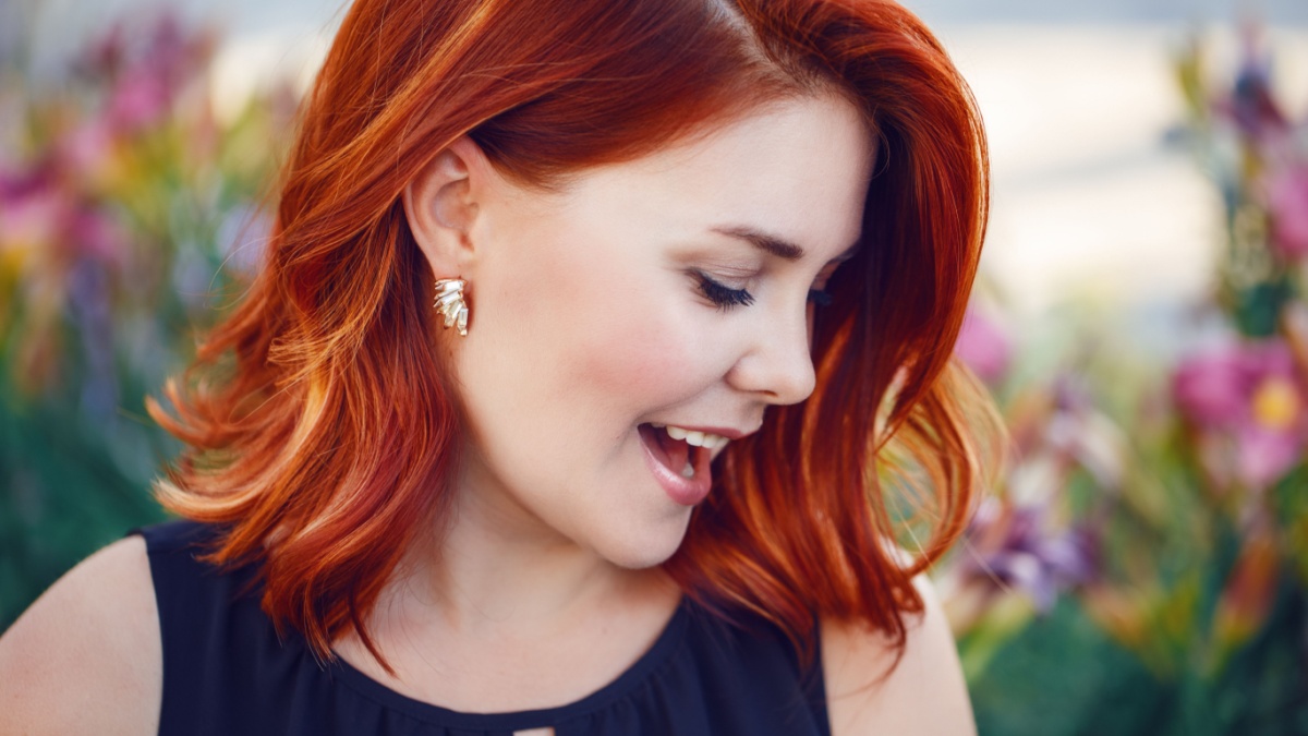 Closeup portrait of smiling laughing flirty middle aged white caucasian woman with waved curly red hair in black dress screaming outside in park, beauty fashion lifestyle concept.