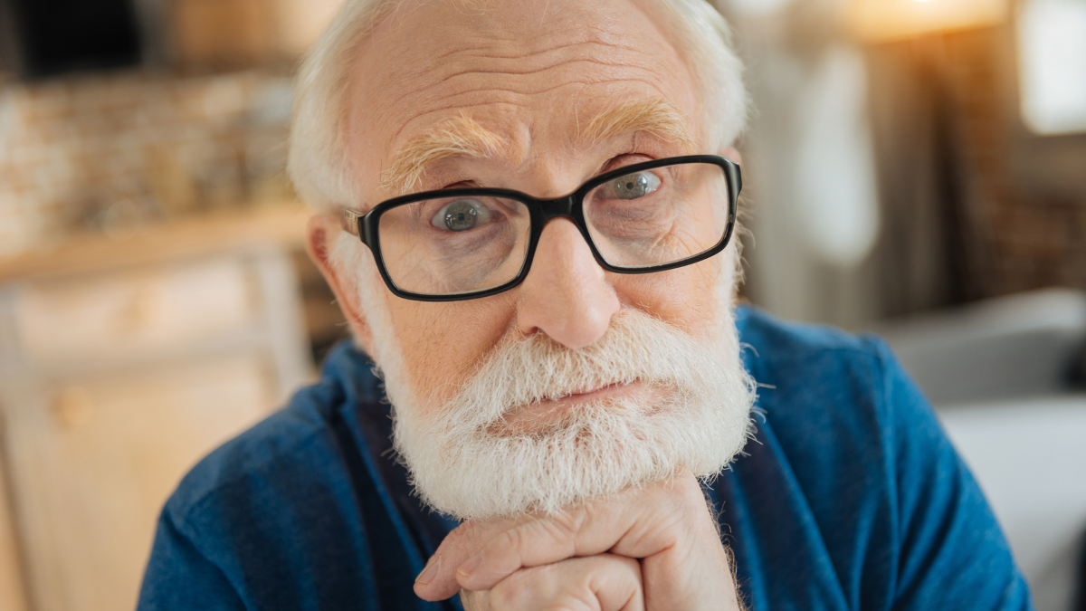 Thoughtful look. Smart nice aged man holding his chin and thinking about life while looking at you.