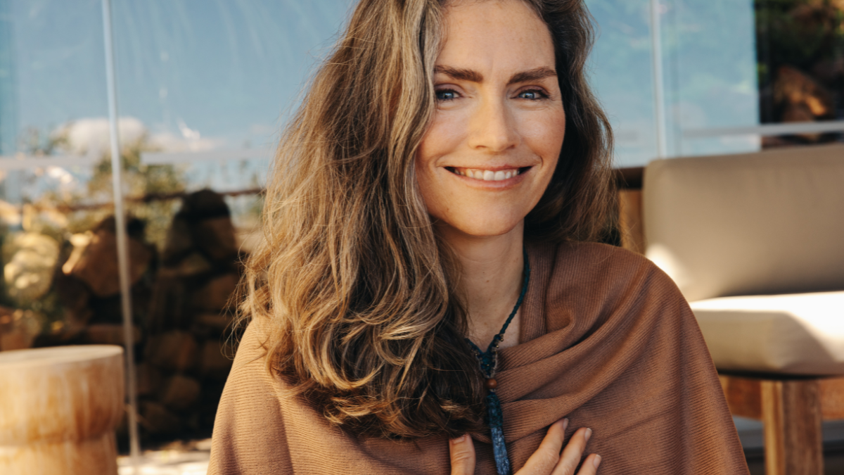 Happy senior woman smiling at the camera while wearing a crystal necklace. Mature woman practicing crystal healing on her chest chakra. Cheerful woman following a holistic lifestyle at home.
