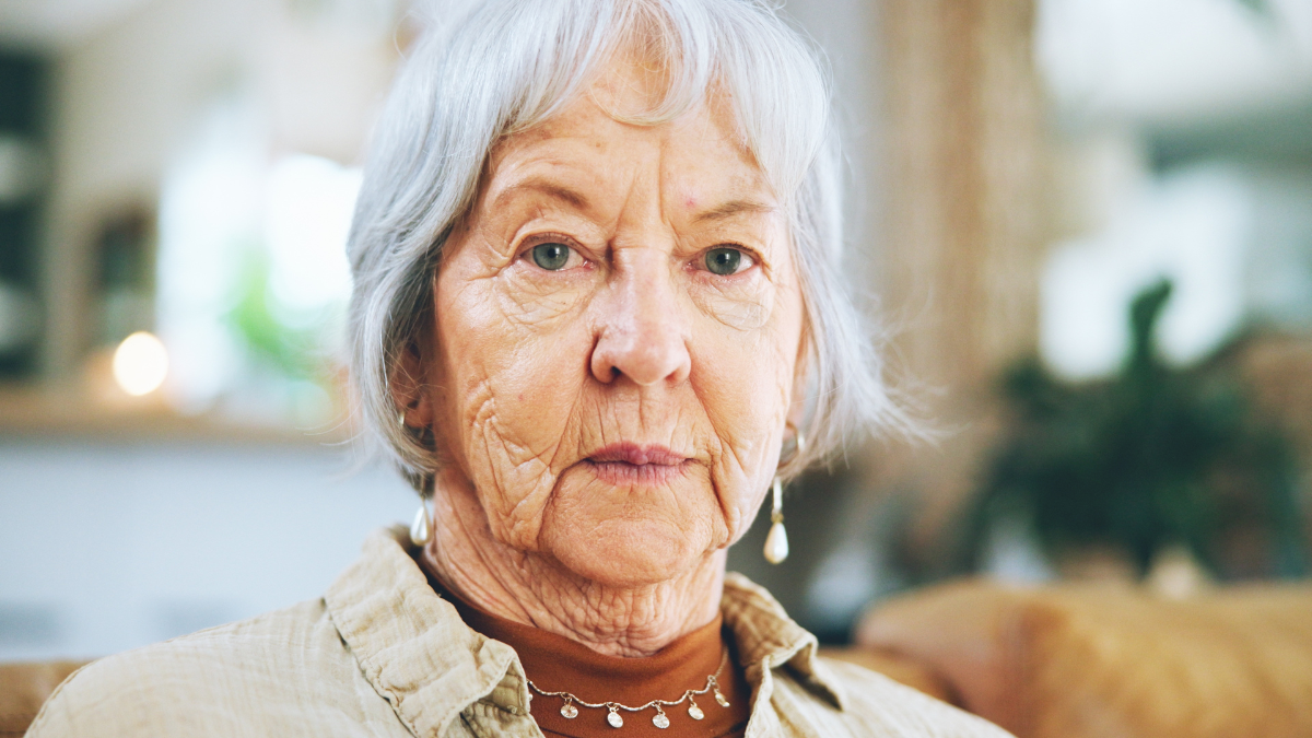 Senior, woman and serious portrait in home with nostalgia, lonely or depression on sofa in retirement. Elderly person, wrinkles and relax from mental health or alzheimers in living room of hospice.
