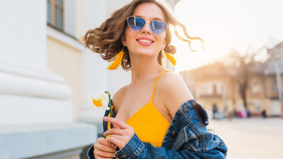 beautiful woman waving hair smiling, stylish apparel, wearing denim jacket and yellow top, fashion trend, summer style, happy positive mood, sunny day, sunrise, street fashion, blue sunglasses.