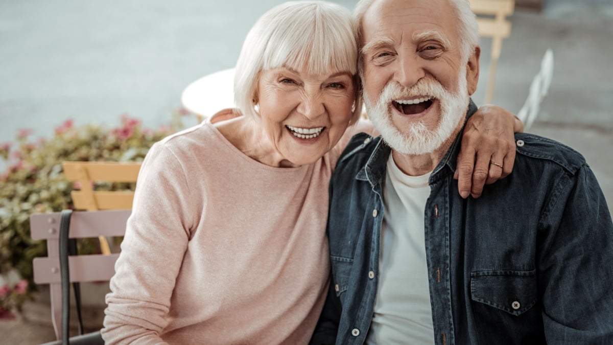 Happy aged couple. Positive aged woman sitting with her husband while hugging him.