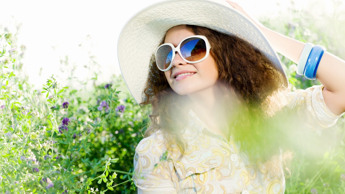 Young beautiful girl in hat and glasses sitting in grass.