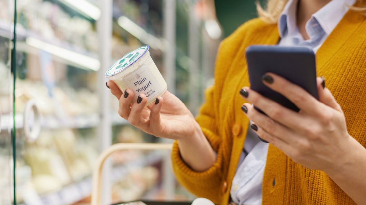 Close up of unrecognizable woman buying dairy products in supermarket and using smartphone, copy space.