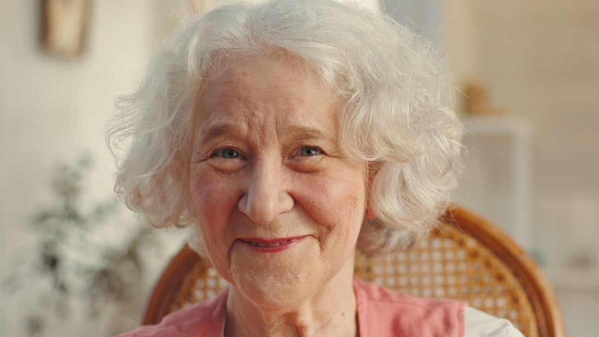 Portrait, elderly woman and smile as pensioner or nursing home for senior care, health and wellness. Female person, retirement and happiness in living room for comfort, relax and rest with confidence.