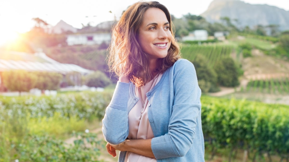 Portrait of mature brunette woman relaxing at park and looking away. Happy woman relaxing outdoor at sunset. Smiling mature woman thinking.