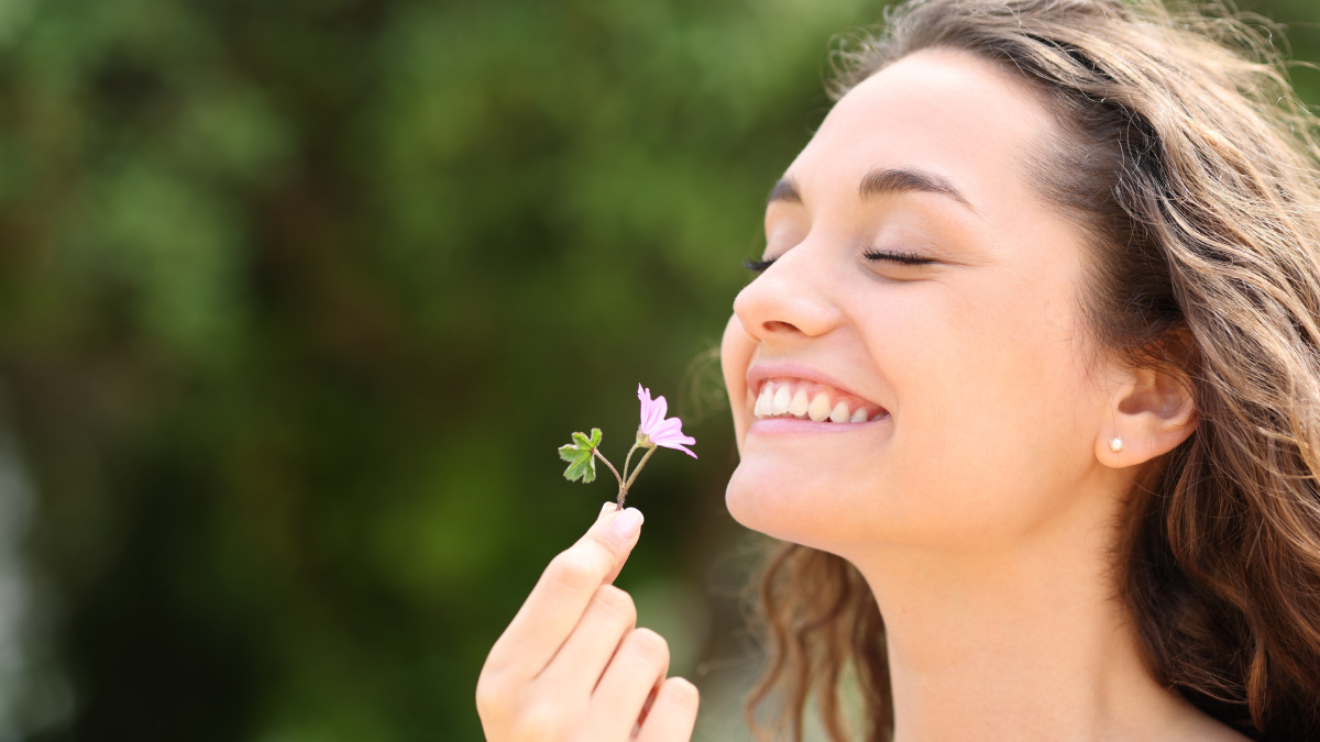 Happy candid woman smelling little flower in a park.