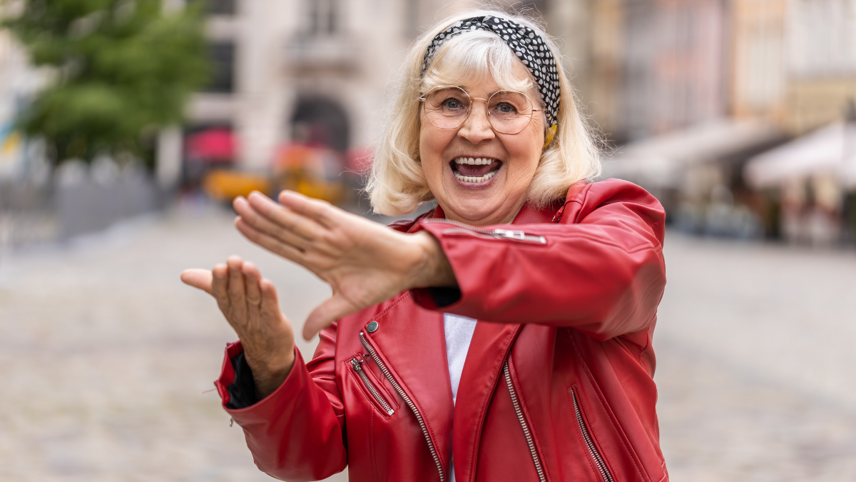 Cheerful rich senior woman showing wasting throwing money around hand gesture, more tips earnings, big profit, win lottery, share, celebrate. Elderly grandmother walking in urban city street outdoors.