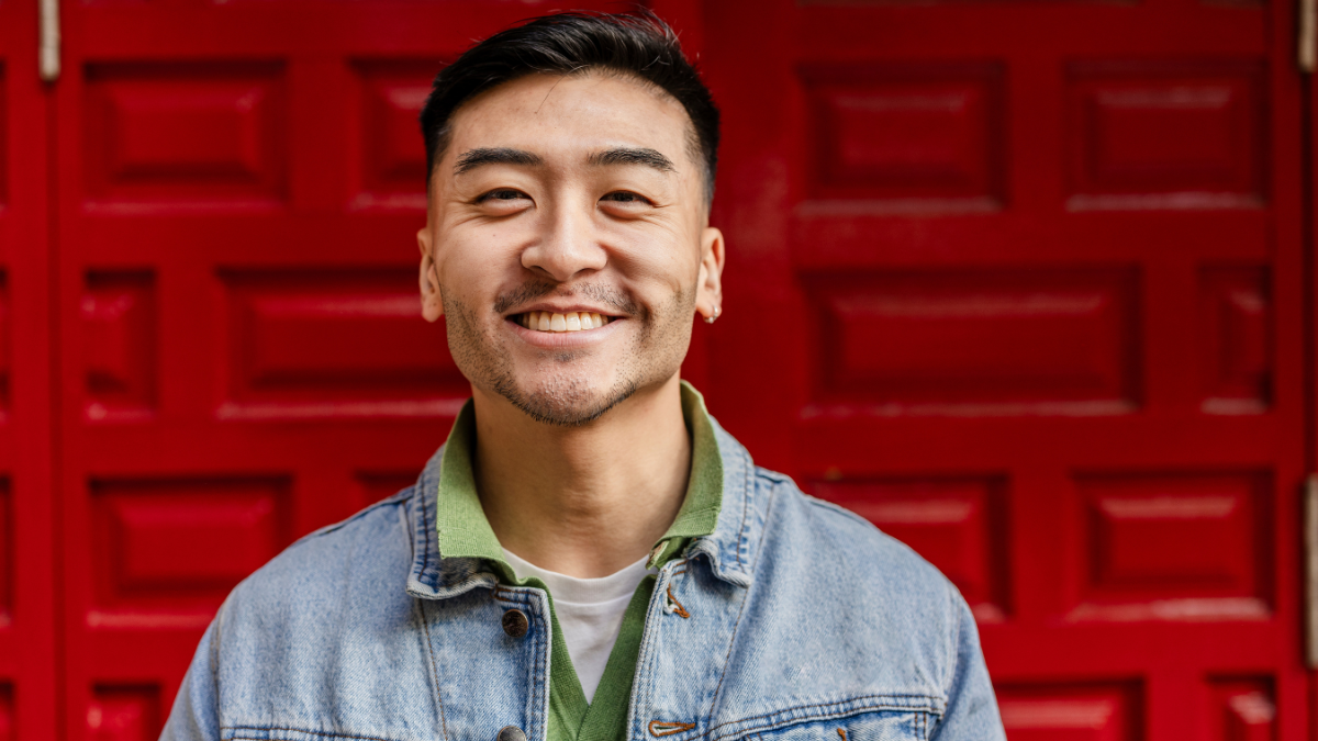 close up portrait of young adult of asian ethnicity looking at camera smiling on colorful red background.