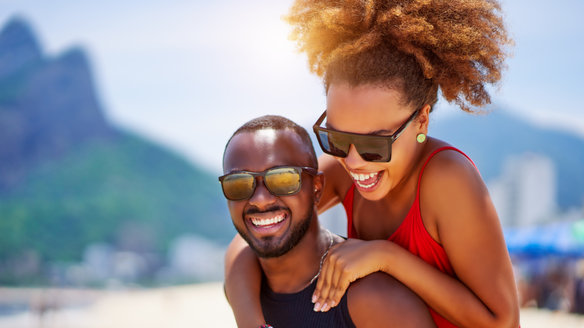 head shot portrait young black brazilian couple in piggyback position having fun in Ipanema beach Brazil.