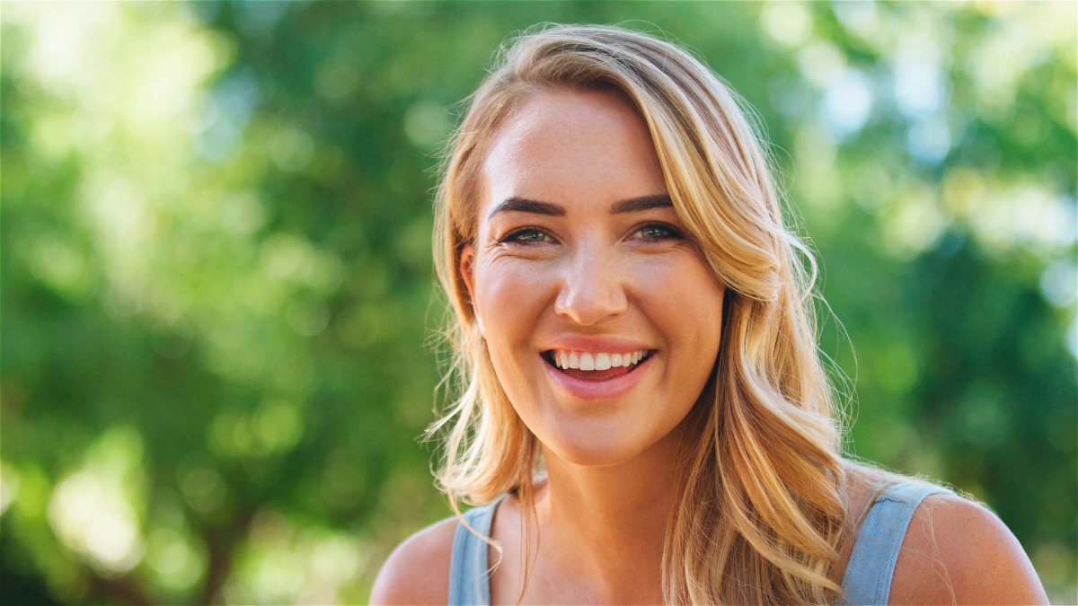 A young woman smiles brightly in a lush green garden.