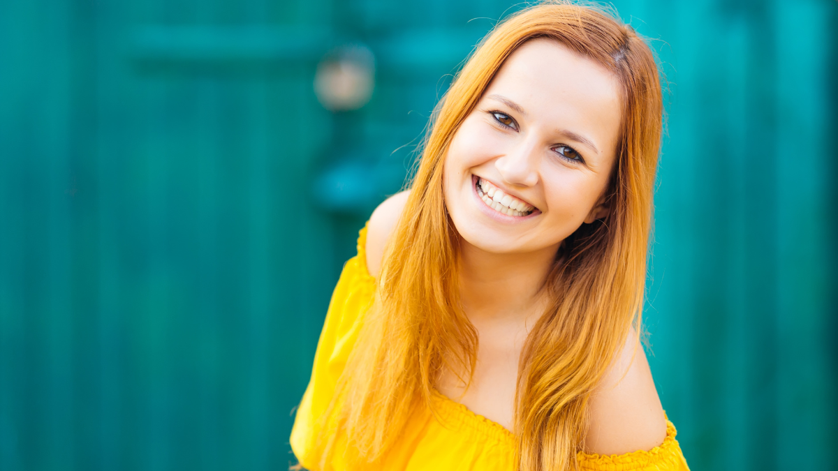 A girl in a beautiful yellow clothes sincere laughs at the background of the wall.