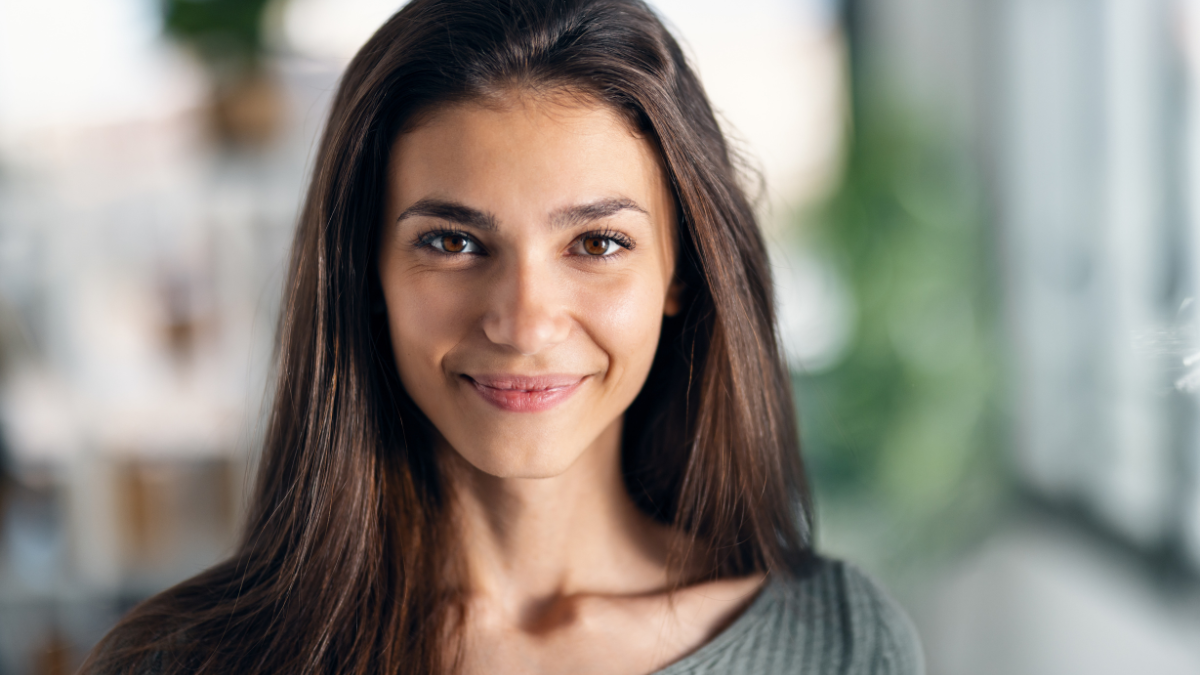 Portrait of kind young woman posing while looking at camera in the living room at home.