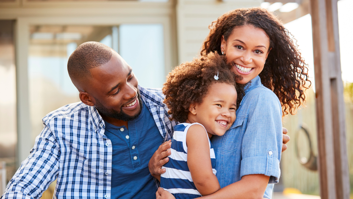 Black family embracing outdoors smiling to camera outside.