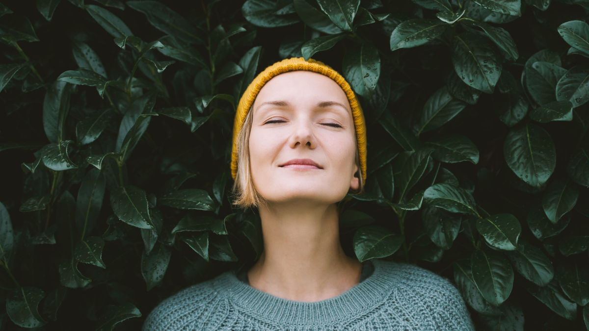 Portrait of relaxed and confident woman with eyes closed on background of green leaves wall. Thoughtful person in front of green hedge. Joy, zen and balance people. Stability through mental health.