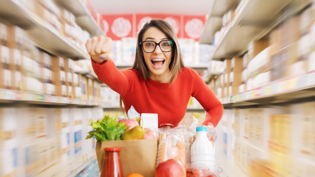 Fast woman with superpowers doing grocery shopping, she is pushing the shopping cart and raising her fist.