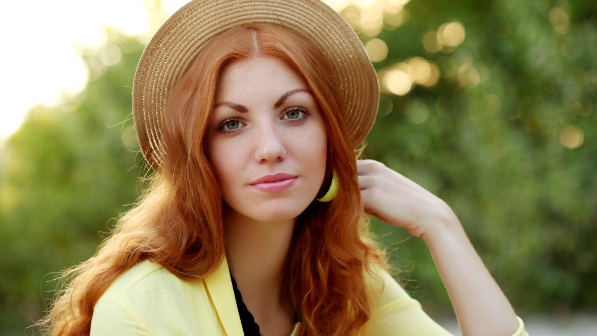 Beautiful red hair young woman wearing yellow cardigan, pencil skirt and hat walking on the street.