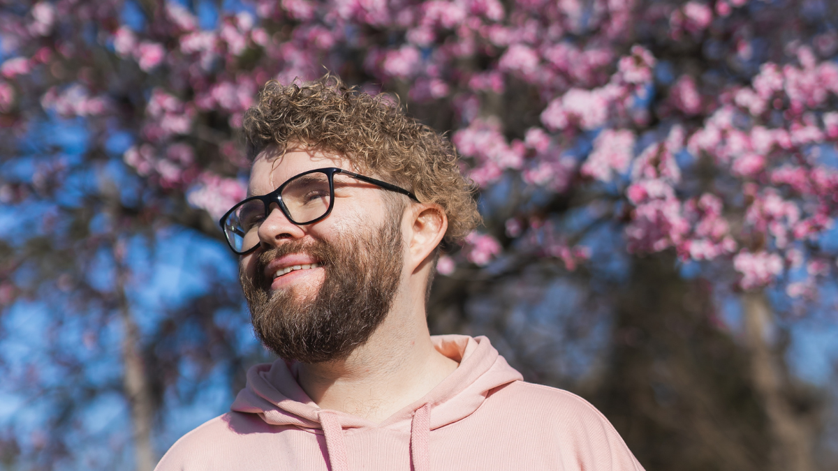 Portrait of happy bearded man smiling in front of blossom tree at springtime.