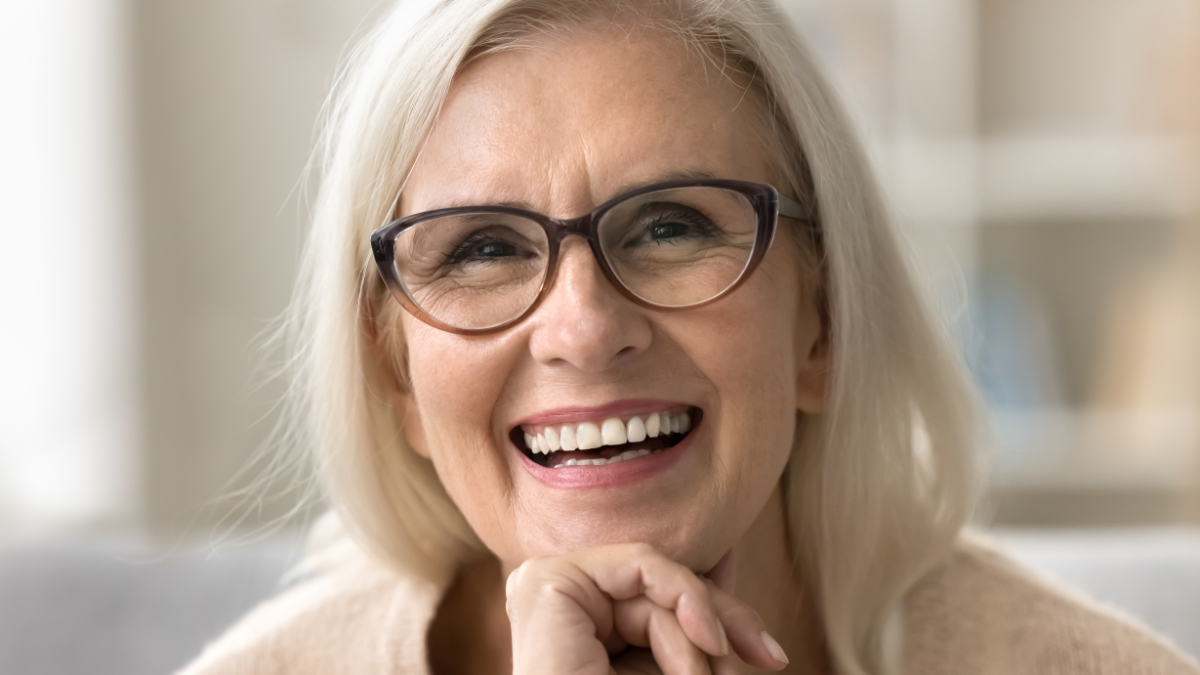Face of happy senior female model with stylish elegant glasses, toothy smile, fair hair. Cheerful old woman looking at camera for close up portrait, laughing, showing healthy white teeth.