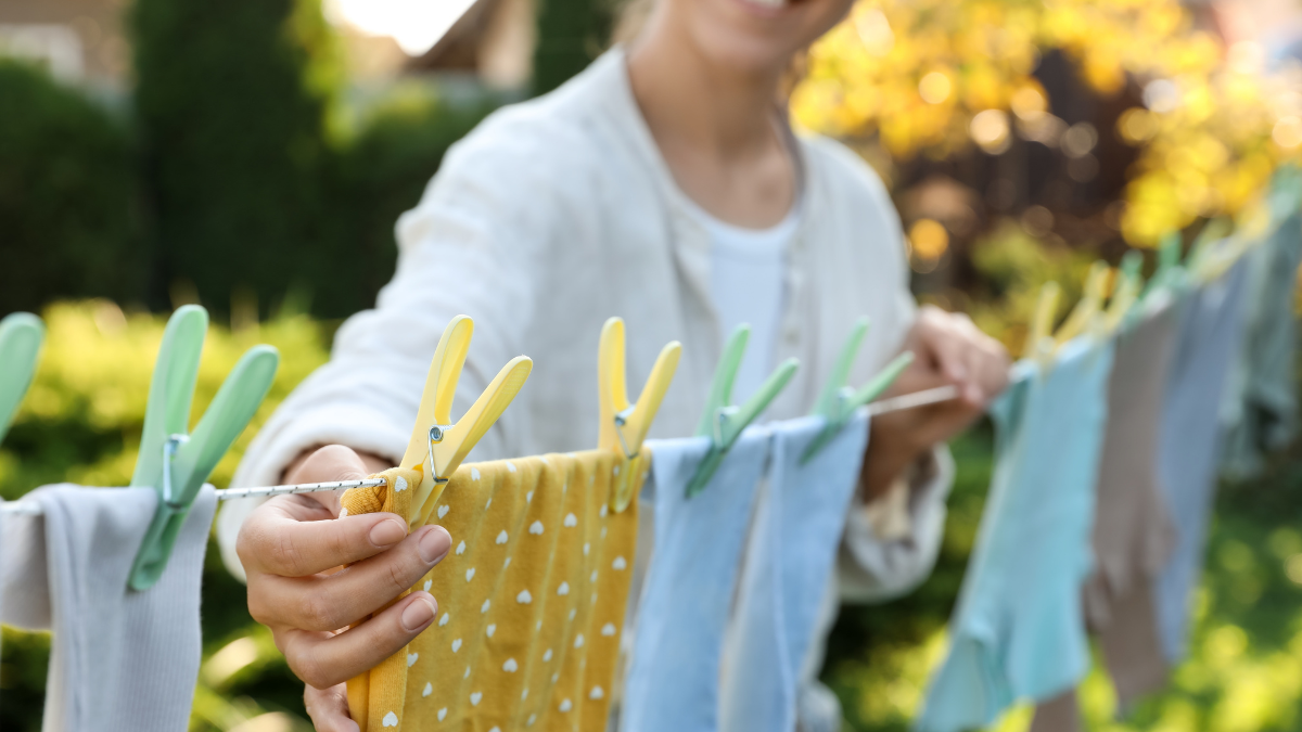 Closeup view of smiling woman hanging baby clothes with clothespins on washing line for drying in backyard.