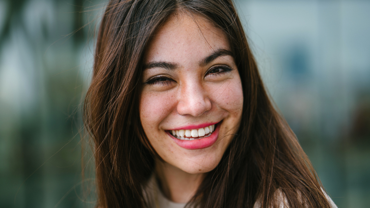 Close up portrait head shot of a young, cute and attractive Japanese Asian woman. She has long brunette hair and beautiful features; she is smiling as she looks into the camera..