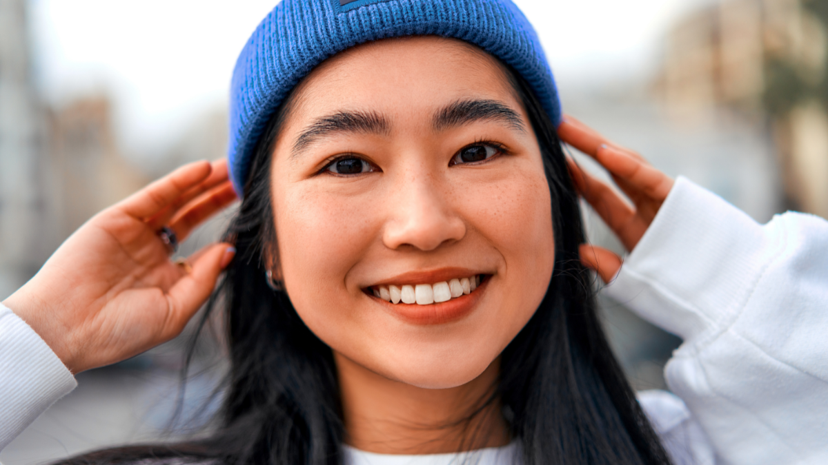 Close-up cute asian young woman in hat standing outdoors and smiling..