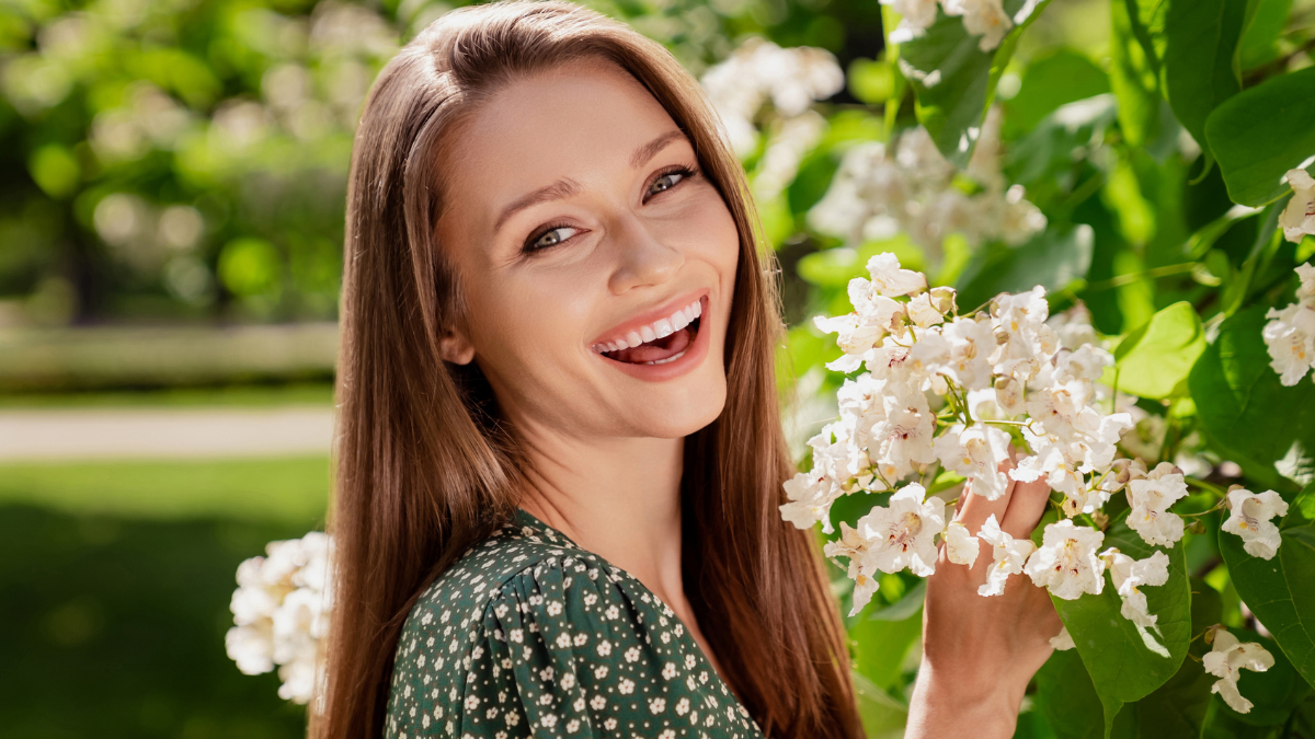 Photo of positive brunette happy cheerful woman smile spring flowers trees enjoy outdoors outside park street.