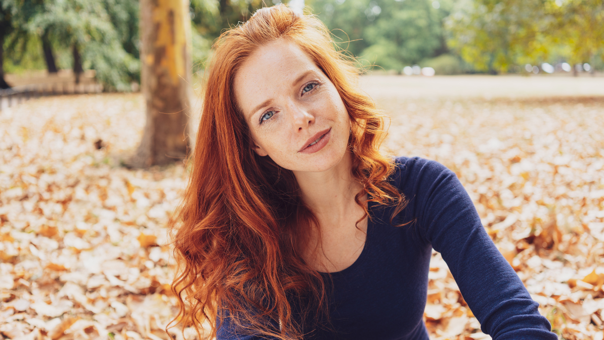 Serious pretty young woman staring at the camera with a thoughtful expression as she relaxes in an autumn park with fallen leaves.
