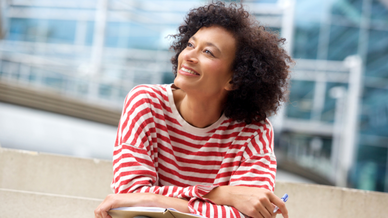 Portrait of happy older woman sitting on steps with book and pen.