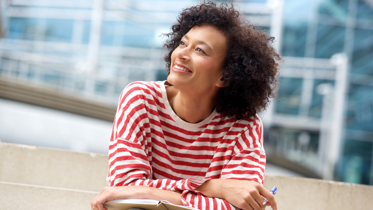 Portrait of happy older woman sitting on steps with book and pen.