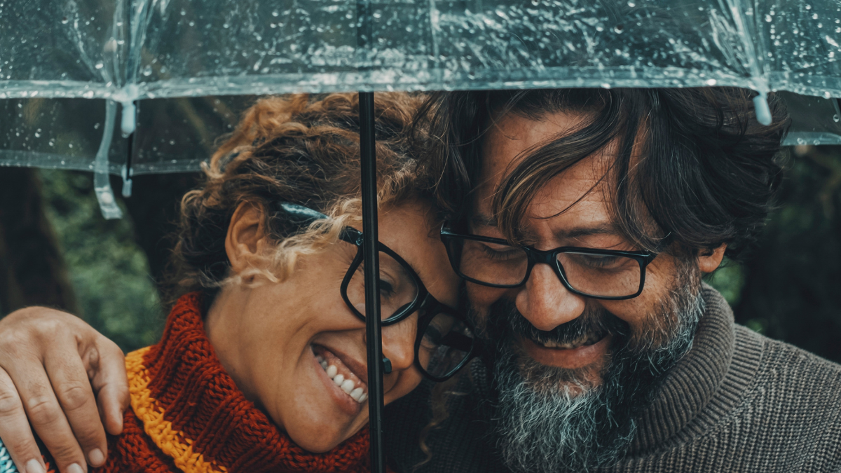 Romantic couple in love under umbrella in rainy day. Man and woman enjoy relationship and happiness together in winter autumn rain. Romance and people smiling end hugging at the park in leisure moment.