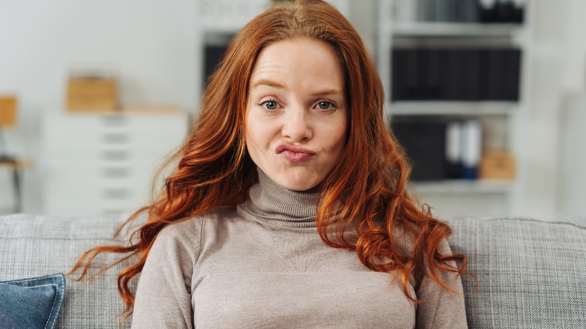 Pretty young redhead woman pulling a funny face making an exaggerated grimace with her lips as she sits on a sofa at home.