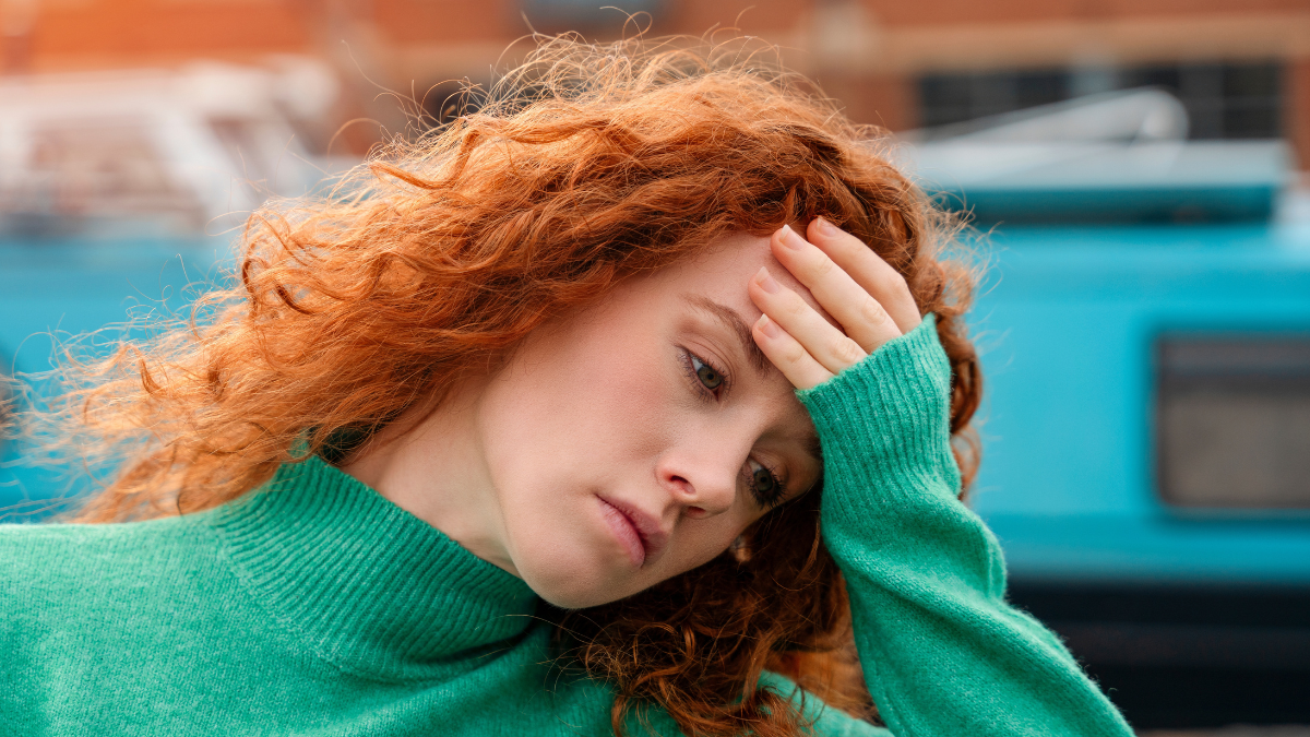 Woman in Green Sweater Sensing Frustration While Standing Outdoors in Urban Setting.