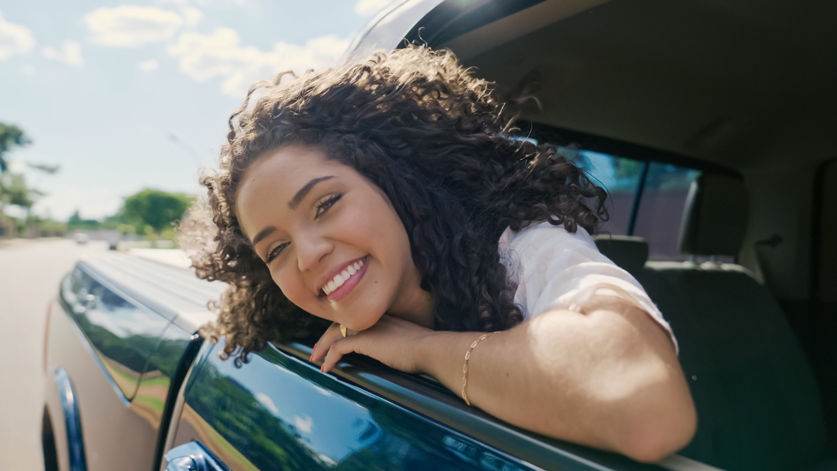 Latin woman in car window. Car trip. Curly hair in wind. Girl looks out of car window.