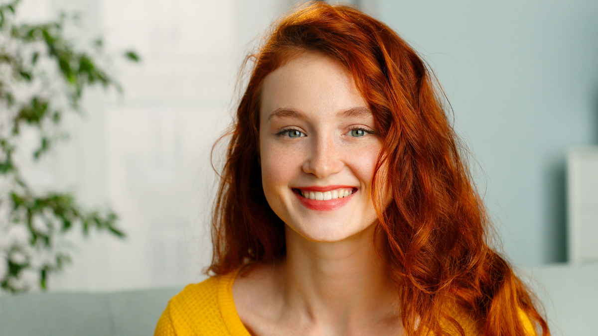 Portrait of beautiful cheerful redhead girl smiling looking at camera sitting on sofa at home.