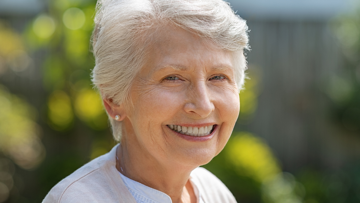 Portrait of serene old woman in garden looking at camera. Closeup portrait of happy older beautiful woman standing outside in summer and smiling. Happy retired senior woman relaxing outdoor..