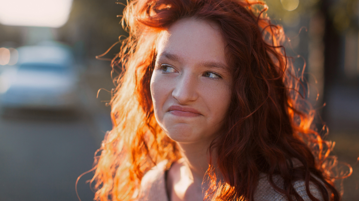 Happy young woman smiling outdoors and walking on city street at sunset time. Portrait of Teen girl with red hair outside.