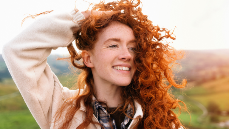 Woman With Red Hair Smiling Outdoors on Sunny Day.