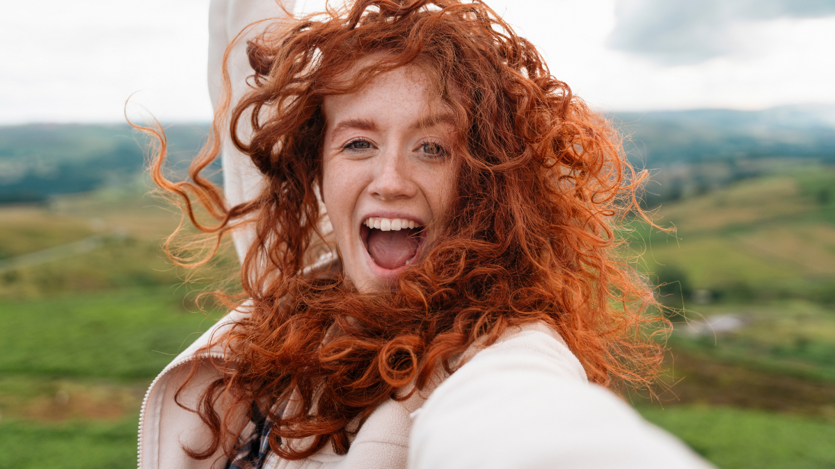 Joyful Young Woman With Curly Red Hair Enjoys Nature at a Scenic Hillside in the Countryside.