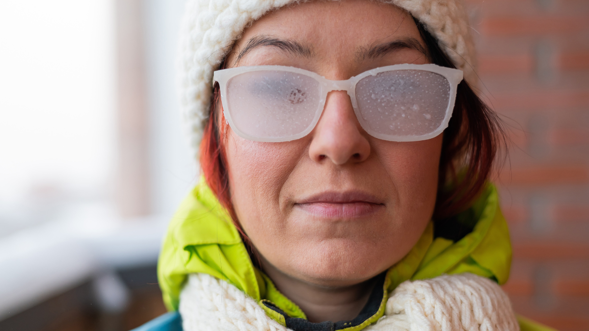 Portrait of a red-haired Caucasian woman in a white knitted hat and icy glasses outside in the frost.